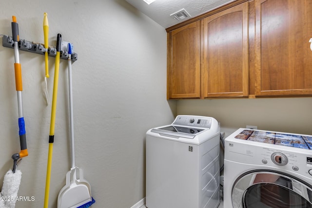 clothes washing area with washer and dryer, cabinet space, and visible vents