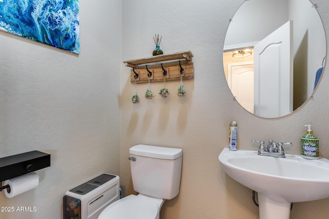 half bathroom featuring toilet, a textured wall, and a sink