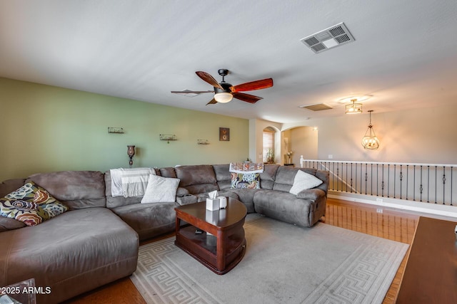 living area featuring wood finished floors, visible vents, arched walkways, and ceiling fan