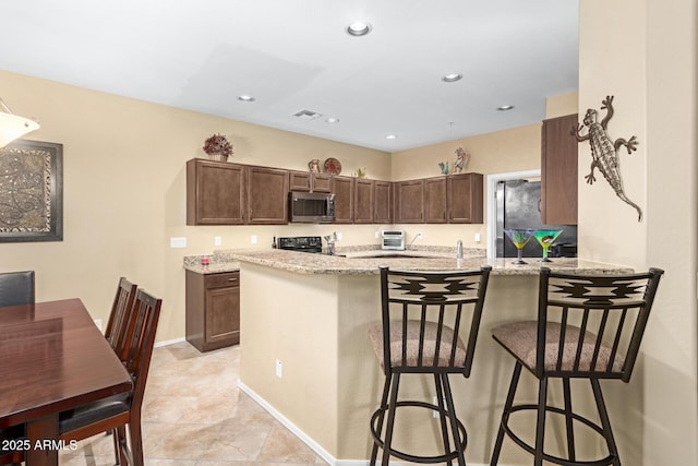 kitchen with light stone countertops, appliances with stainless steel finishes, a kitchen bar, and kitchen peninsula