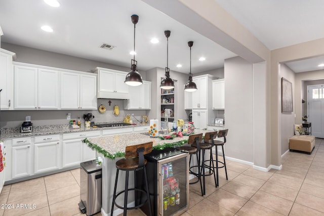 kitchen featuring white cabinets, stainless steel gas stovetop, light stone countertops, and hanging light fixtures