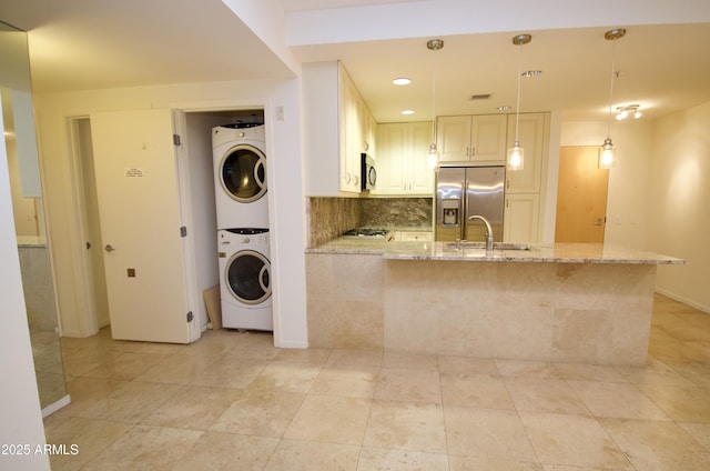 kitchen with tasteful backsplash, hanging light fixtures, stacked washer and clothes dryer, stainless steel appliances, and light stone countertops