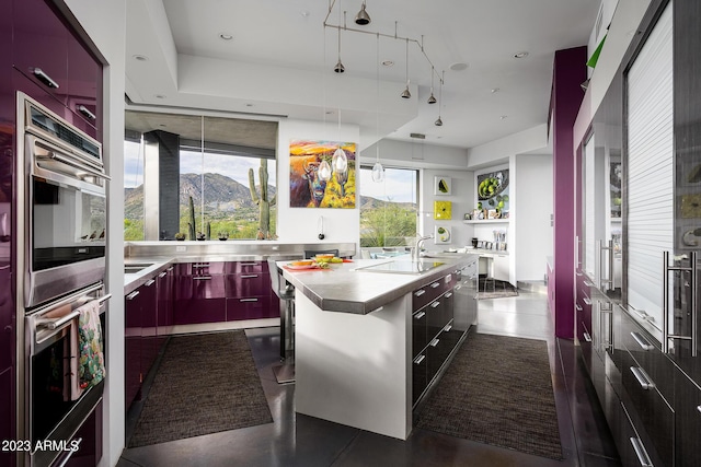 kitchen featuring a wealth of natural light, a breakfast bar, stainless steel double oven, a center island with sink, and a mountain view