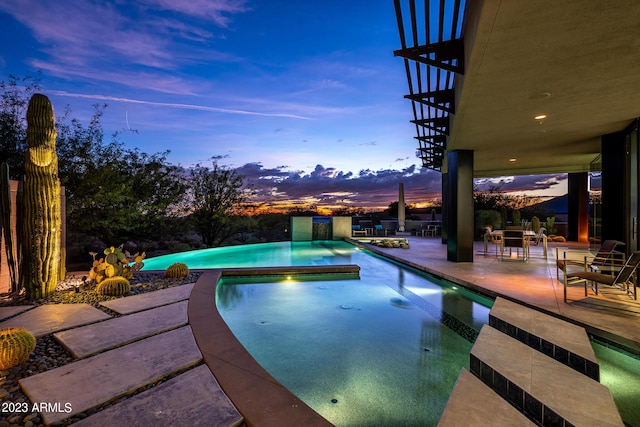 pool at dusk with a patio area and an in ground hot tub