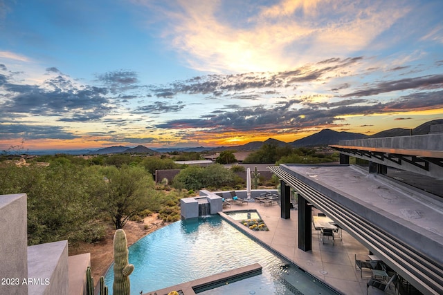 pool at dusk featuring a mountain view, a bar, pool water feature, and a patio