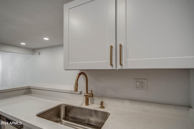 details with white cabinetry, light stone counters, and sink