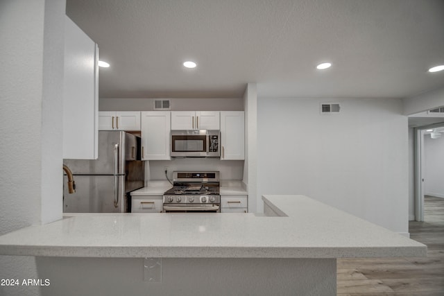 kitchen featuring appliances with stainless steel finishes, kitchen peninsula, white cabinetry, and light hardwood / wood-style flooring