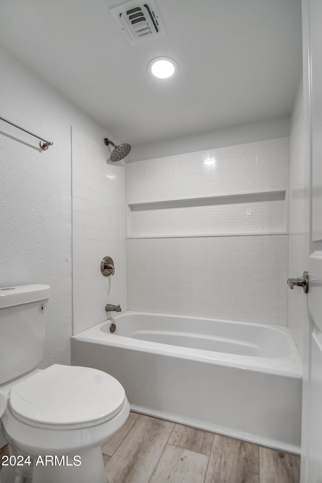 bathroom featuring wood-type flooring, tiled shower / bath combo, and toilet