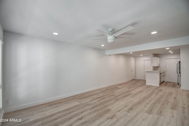 basement with light wood-type flooring, a textured ceiling, fridge, ceiling fan, and sink