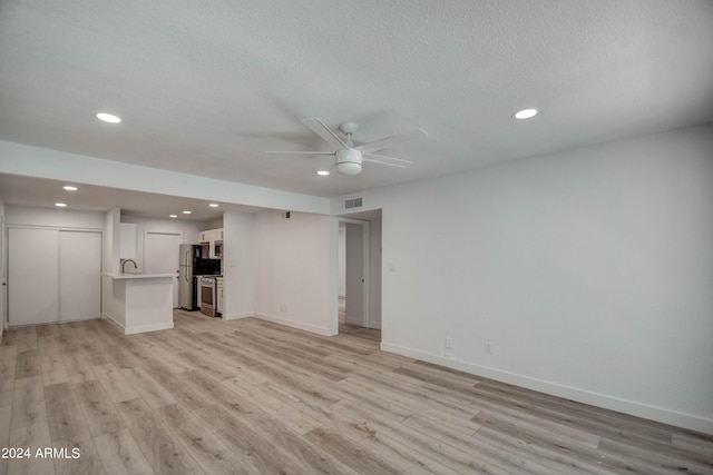 unfurnished living room featuring ceiling fan, a textured ceiling, and light hardwood / wood-style flooring