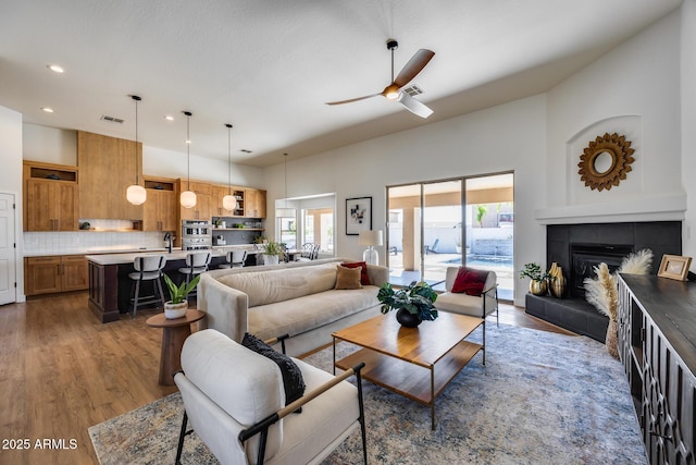 living area with ceiling fan, wood finished floors, visible vents, and a tile fireplace