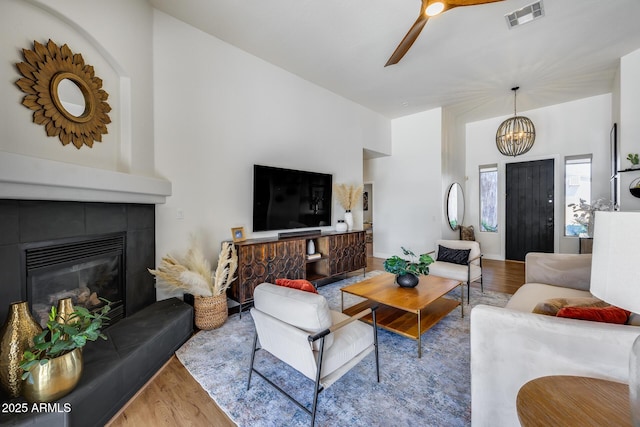 living area featuring visible vents, wood finished floors, a fireplace, and ceiling fan with notable chandelier