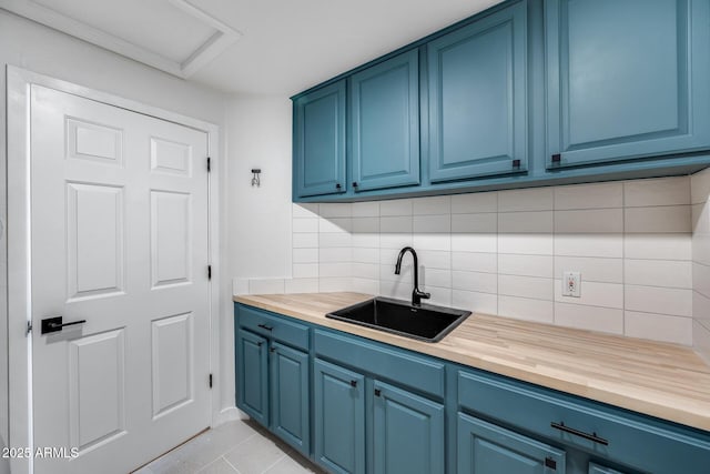 kitchen with light tile patterned flooring, a sink, decorative backsplash, wood counters, and blue cabinets