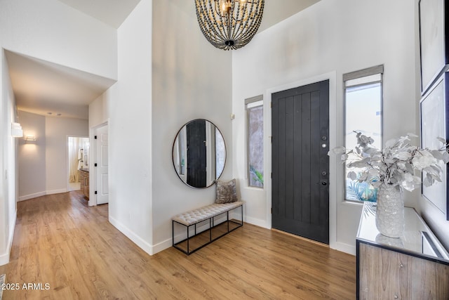 foyer with a notable chandelier, baseboards, a high ceiling, and light wood-style floors