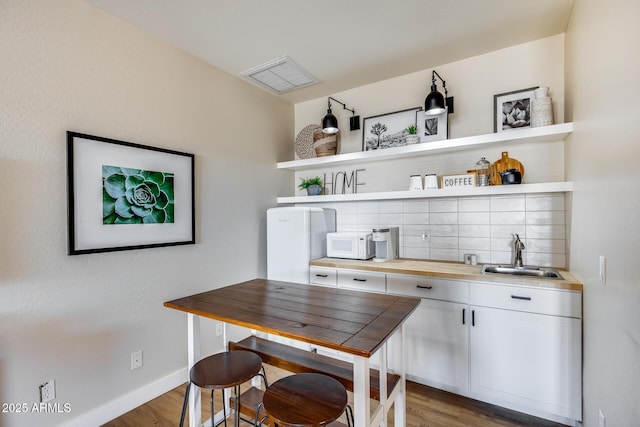 kitchen featuring open shelves, decorative backsplash, white microwave, and a sink