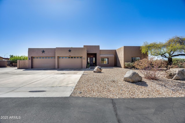 pueblo-style house featuring stucco siding, a garage, and driveway