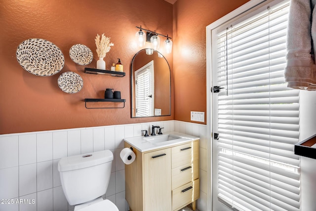 half bath featuring vanity, toilet, and wainscoting