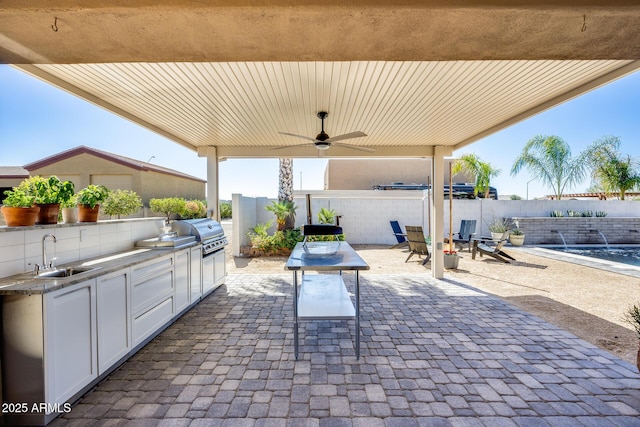 view of patio with a ceiling fan, fence, exterior kitchen, a sink, and grilling area