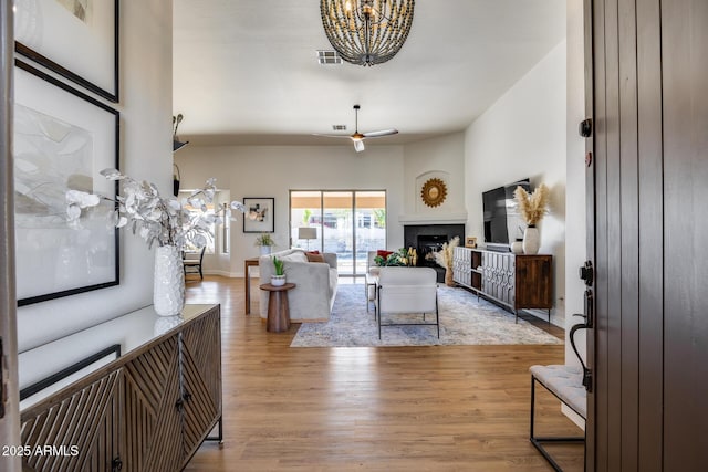 living room with visible vents, ceiling fan with notable chandelier, light wood-style floors, a fireplace, and baseboards