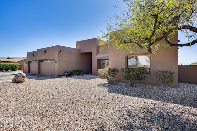 pueblo-style house featuring stucco siding, concrete driveway, an attached garage, and fence