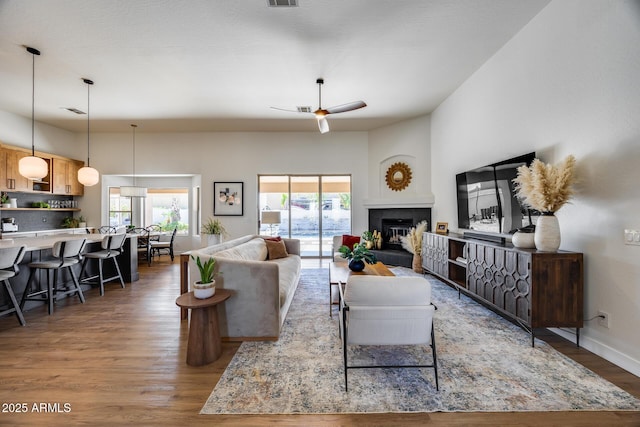 living room featuring a ceiling fan, visible vents, wood finished floors, baseboards, and a tile fireplace