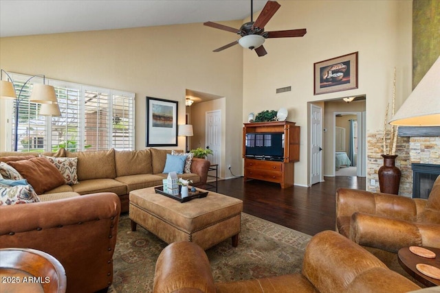 living room with visible vents, a ceiling fan, lofted ceiling, wood finished floors, and a stone fireplace