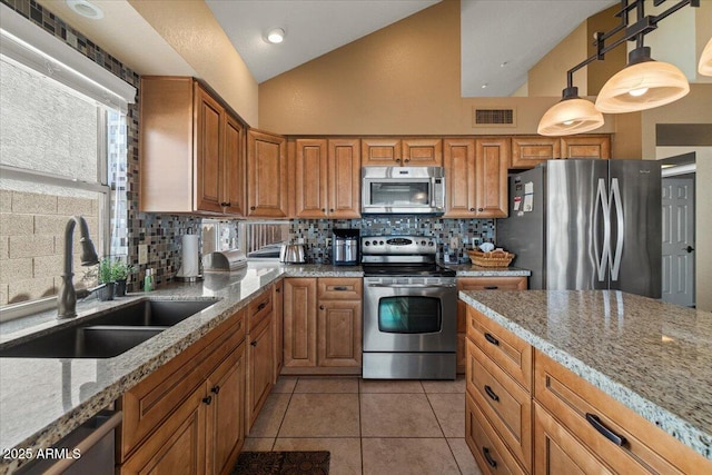 kitchen featuring visible vents, lofted ceiling, light stone countertops, stainless steel appliances, and a sink