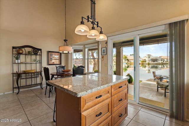 kitchen with a kitchen island, a water view, light stone countertops, pendant lighting, and light tile patterned flooring