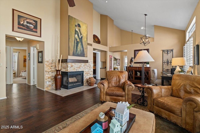 living room with high vaulted ceiling, a stone fireplace, wood-type flooring, and baseboards