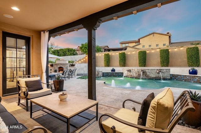 pool at dusk featuring an outdoor stone fireplace, pool water feature, and a patio area