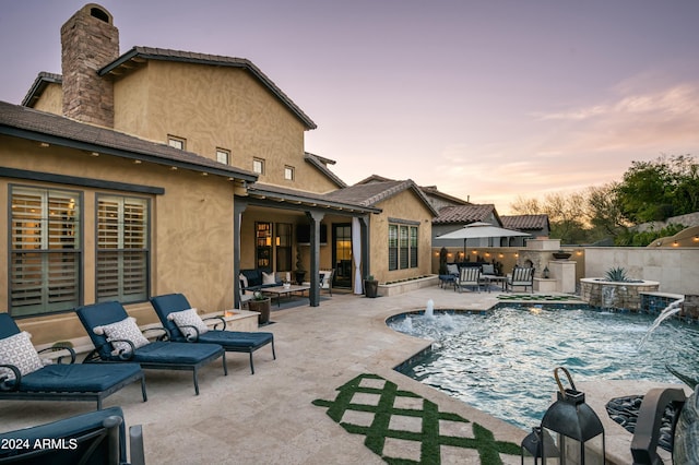 pool at dusk featuring pool water feature, a patio area, and exterior kitchen