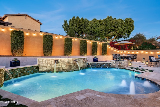 pool at dusk with pool water feature and a patio