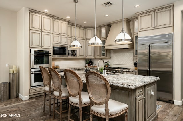 kitchen with light stone countertops, built in appliances, dark hardwood / wood-style floors, and an island with sink