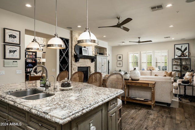 kitchen featuring sink, light stone counters, dark hardwood / wood-style flooring, decorative light fixtures, and a fireplace