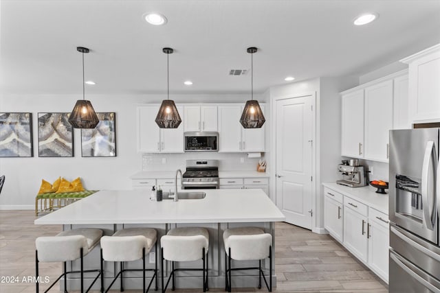 kitchen featuring white cabinetry, hanging light fixtures, stainless steel appliances, a center island with sink, and light hardwood / wood-style flooring