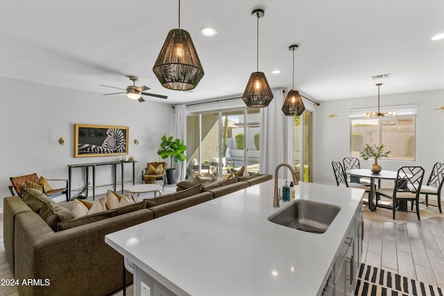 kitchen featuring a kitchen island with sink, sink, decorative light fixtures, and light hardwood / wood-style flooring