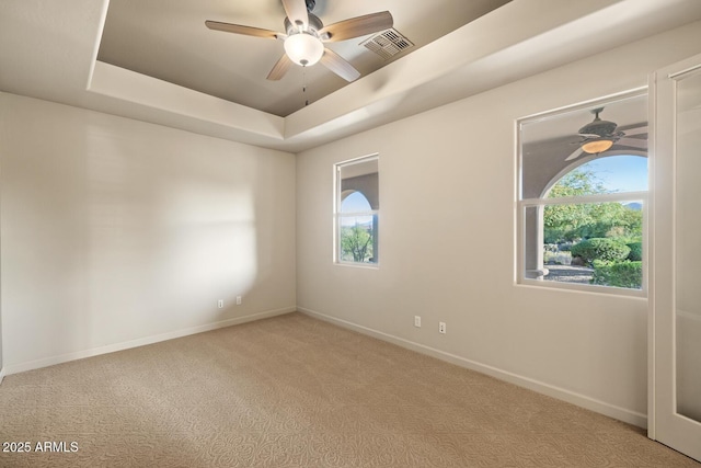 spare room featuring a raised ceiling, carpet, a ceiling fan, baseboards, and visible vents