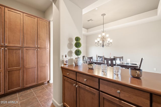 kitchen featuring visible vents, a chandelier, brown cabinets, dark tile patterned flooring, and hanging light fixtures
