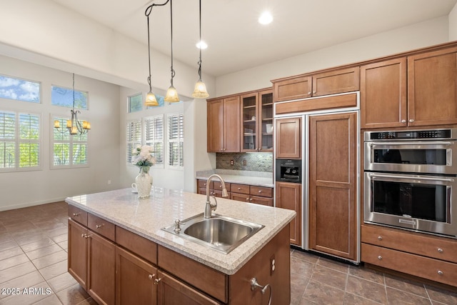 kitchen featuring brown cabinets, a sink, double oven, paneled fridge, and an island with sink