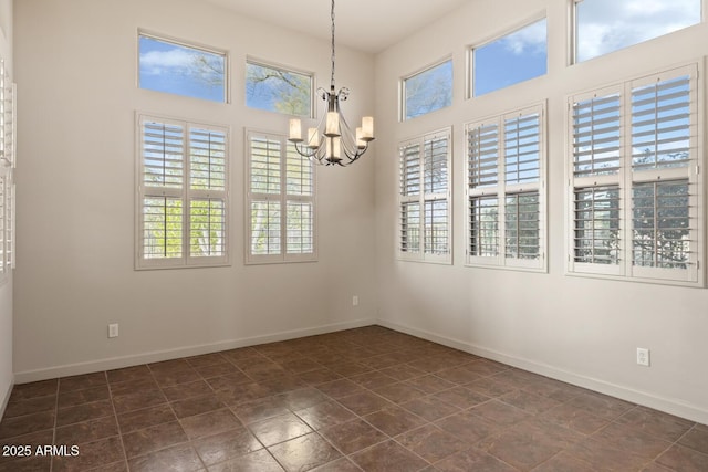 spare room featuring an inviting chandelier, baseboards, and a towering ceiling