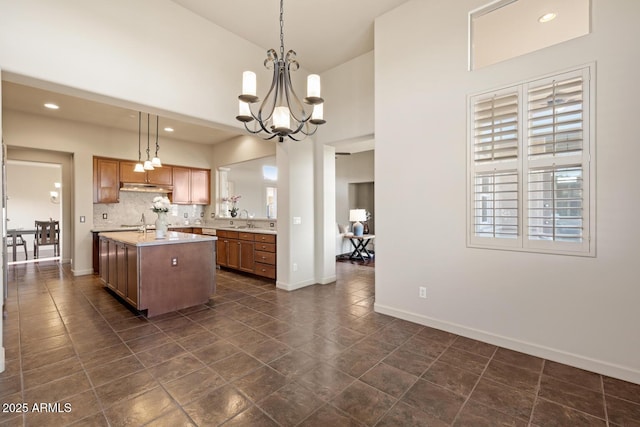 kitchen with a notable chandelier, a sink, a kitchen island with sink, light countertops, and under cabinet range hood