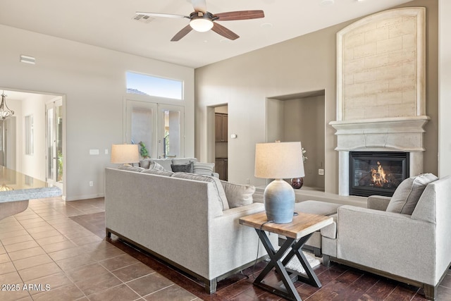 living area with a glass covered fireplace, dark tile patterned floors, ceiling fan, and visible vents