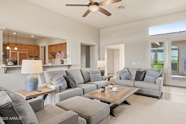 living area featuring a ceiling fan, visible vents, light wood-type flooring, and a towering ceiling