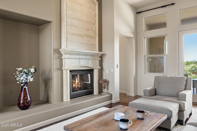 living area with a glass covered fireplace, baseboards, and wood finished floors