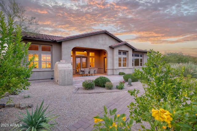 back of house at dusk with a patio and stucco siding