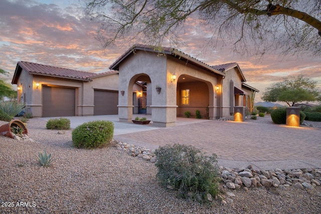 mediterranean / spanish home with an attached garage, driveway, a tile roof, and stucco siding