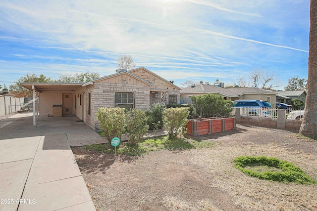 view of front of home with stone siding, an attached carport, concrete driveway, and fence