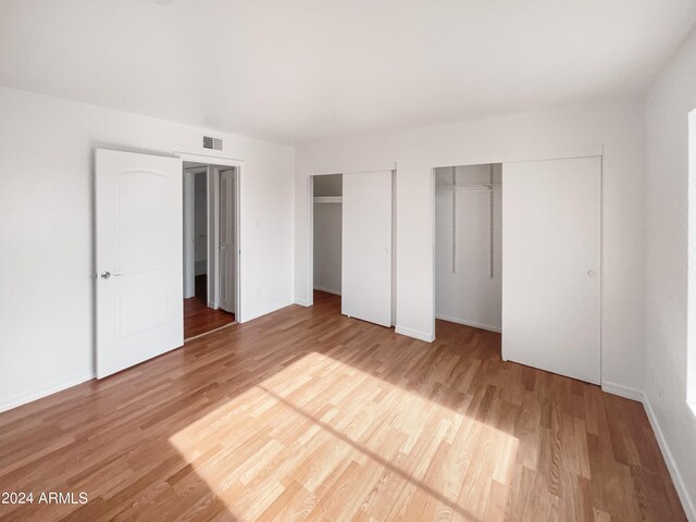 unfurnished bedroom with multiple closets and wood-type flooring