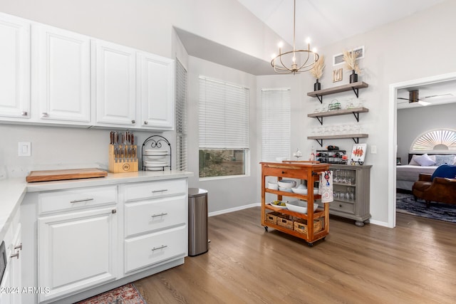 kitchen featuring hanging light fixtures, white cabinets, ceiling fan with notable chandelier, light wood-type flooring, and lofted ceiling