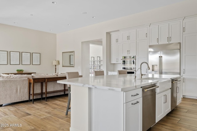 kitchen with appliances with stainless steel finishes, white cabinets, open floor plan, light wood-style flooring, and an island with sink